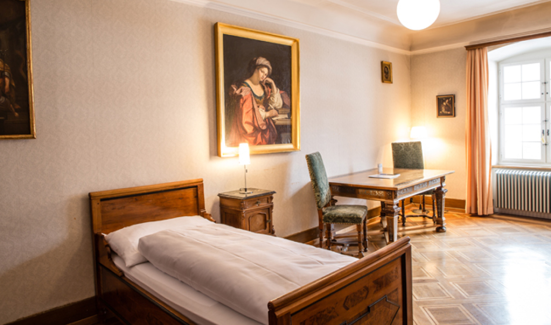 Zimmer in der Gastabteilung im Kloster Engelberg mit einem Bett und einem Schreibtisch.